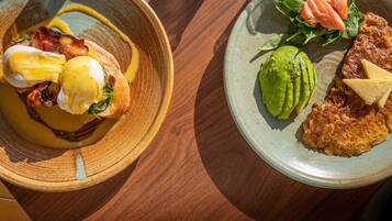 A wooden table with two plates of food, one with eggs Benedict and the other with a salad and avocado.
