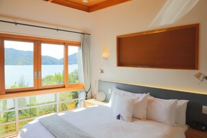 Quarto com uma cama grande, vista para um lago e teto de madeira.