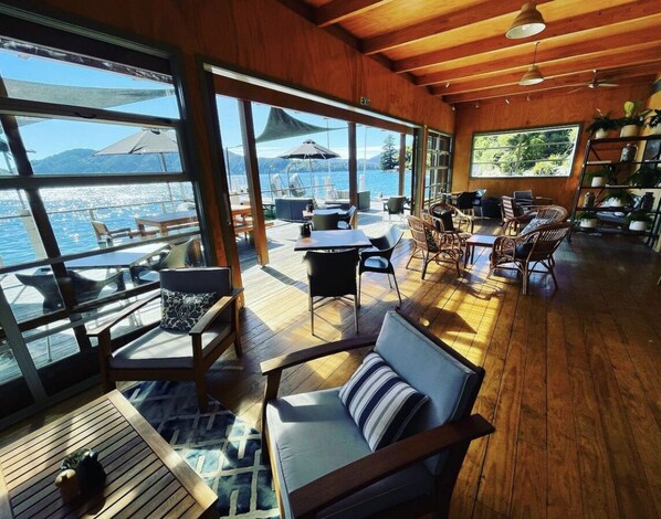 A spacious deck with wooden flooring, large windows offering a view of the sea, and various seating arrangements including chairs and a sofa.