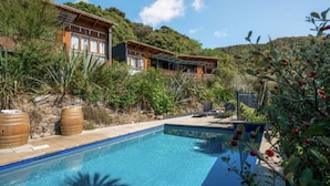 Eine moderne Villa mit Swimmingpool, umgeben von üppiger Vegetation und Hügeln.