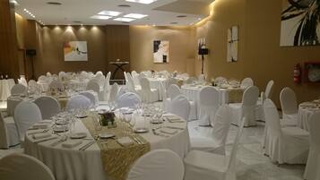 Un salón de banquetes con mesas redondas dispuestas para comer, sillas blancas y obras de arte en las paredes.
