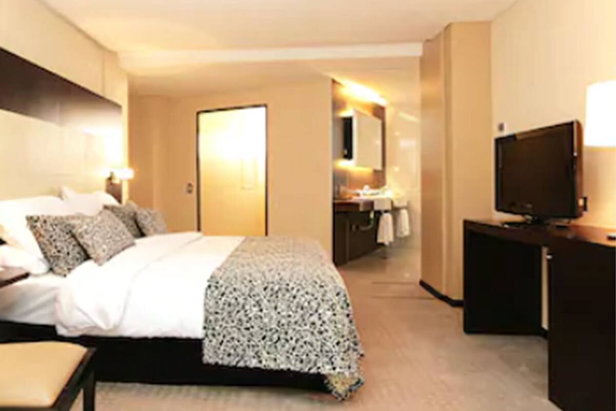 Une chambre d’hôtel avec un lit, une table de chevet, une télévision et une salle de bain visible à travers une porte ouverte.