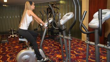 Una mujer usando una máquina elíptica en un gimnasio con alfombra estampada y equipo de ejercicio.