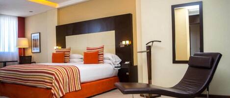 A hotel room with a bed, a chair, a nightstand, a lamp, and a mirror.
