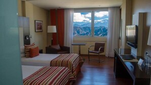 A hotel room with two beds, a TV, a desk, a chair, a lamp, and a window with a mountain view. - Del Bono Park Hotel Spa & Casino (San Juan)