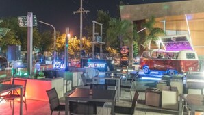 An outdoor seating area with tables and chairs, a food truck, and a building with illuminated signage. - Del Bono Park Hotel Spa & Casino (San Juan)