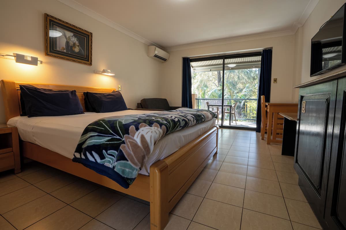 Habitación de hotel con cama, mesita de noche, aire acondicionado y vistas al exterior a través de una puerta corrediza.