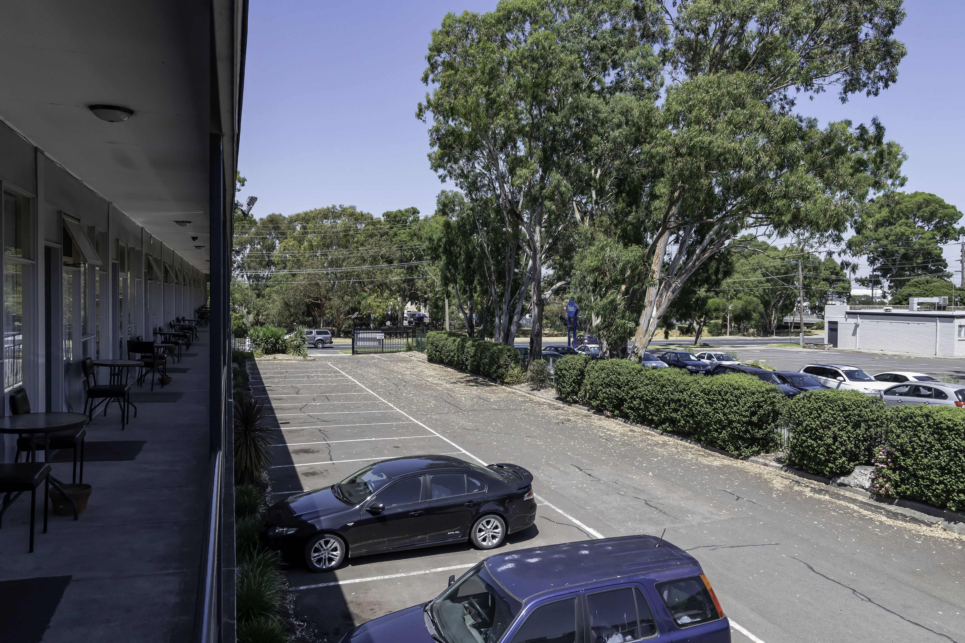 A parking lot with several cars, a building with outdoor seating, and trees in the background.