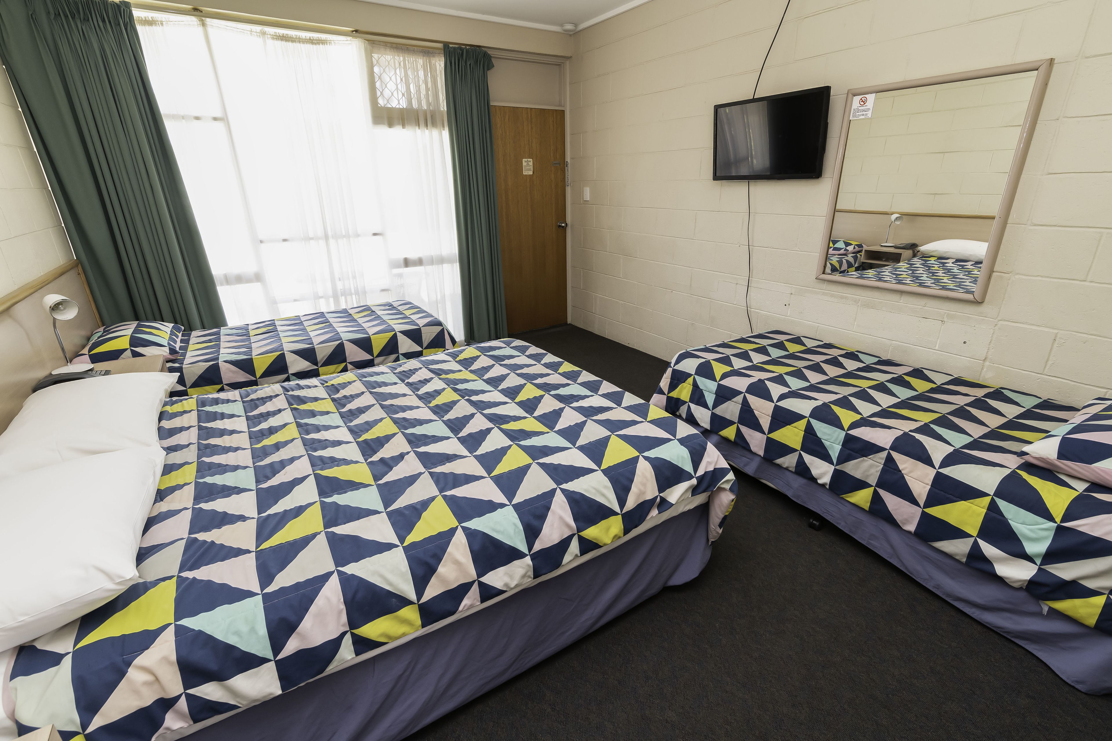 A room with two beds, a TV mounted on the wall, and a door leading to another room.