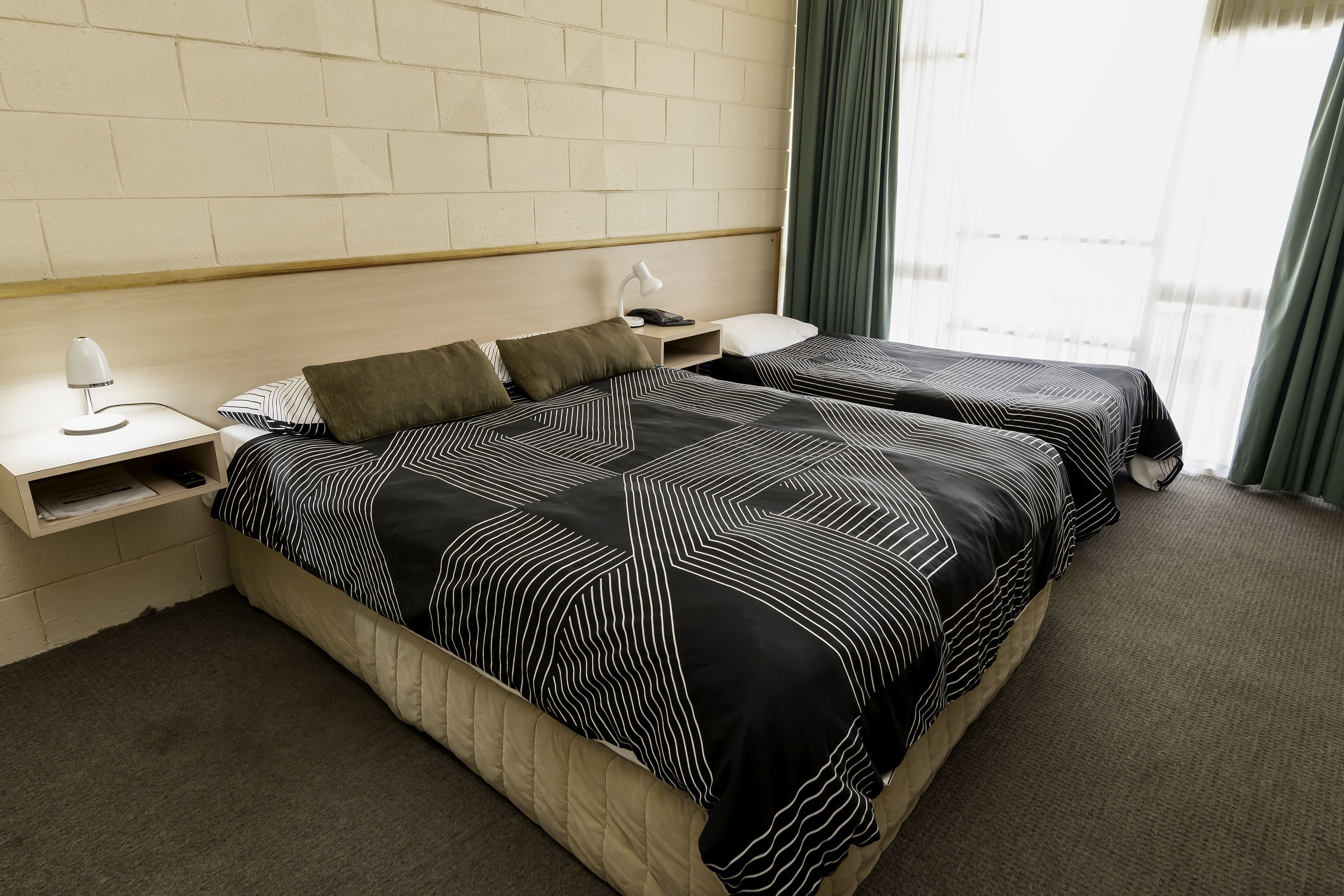 A hotel room with two beds, a nightstand, a lamp, and a window with curtains.