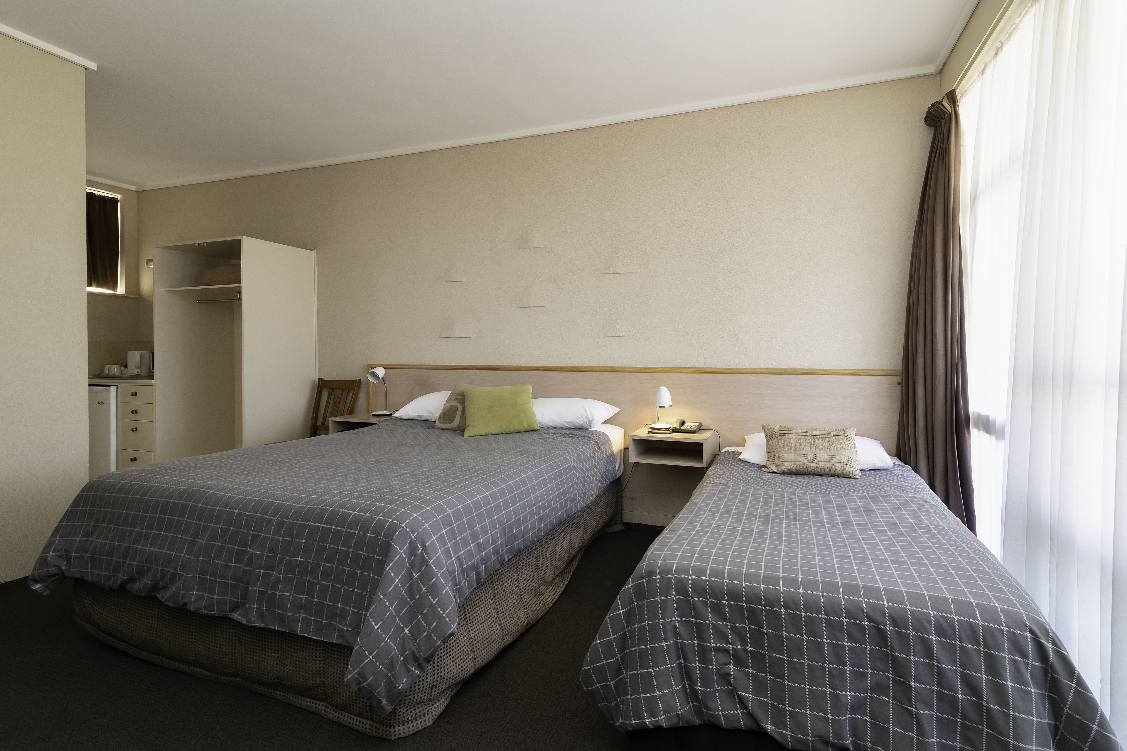 Une chambre d’hôtel avec deux lits, une armoire, un bureau et une fenêtre avec des rideaux.