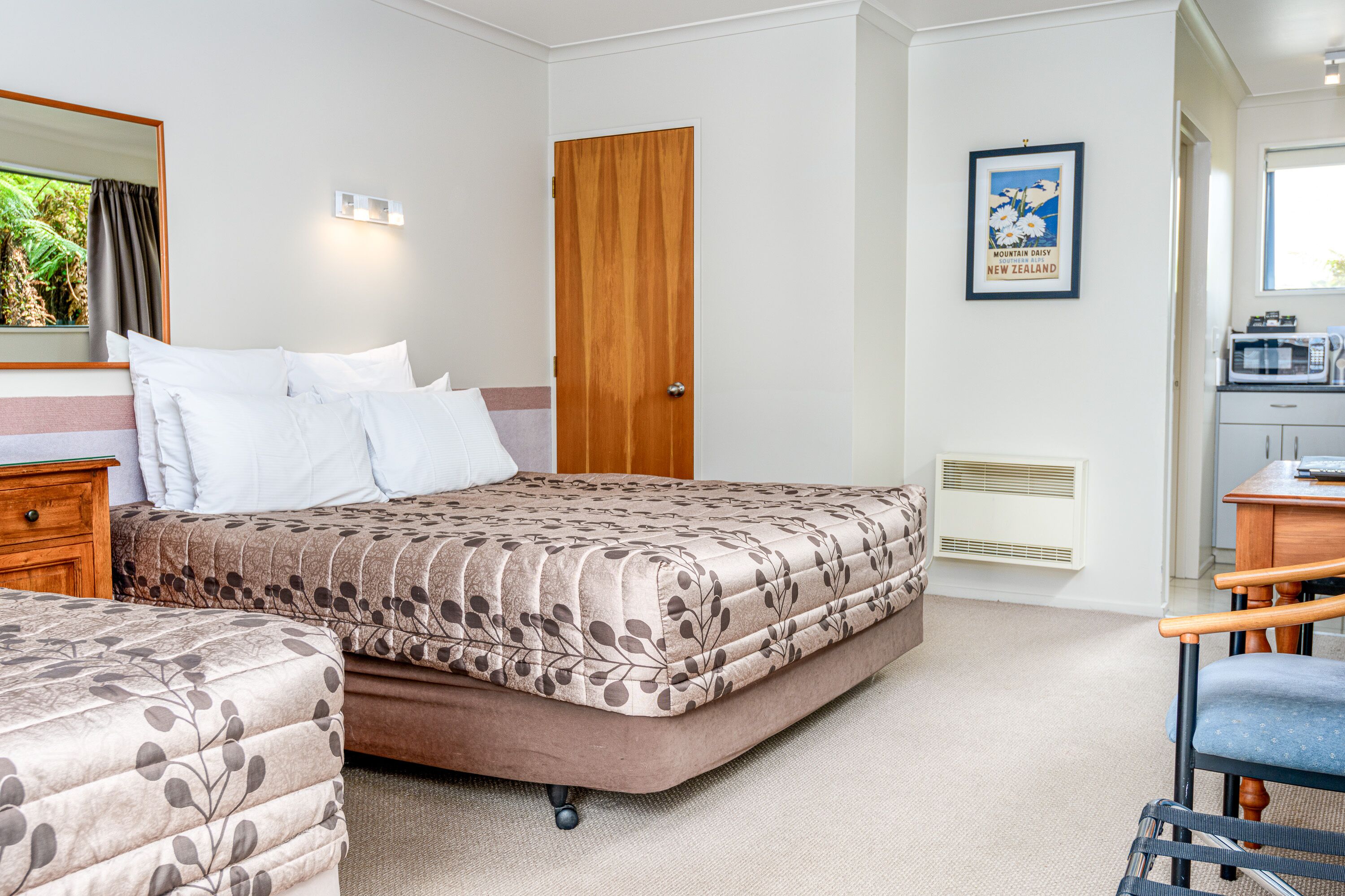 A bedroom with two beds, a wooden door, a framed picture, a desk, and a chair.