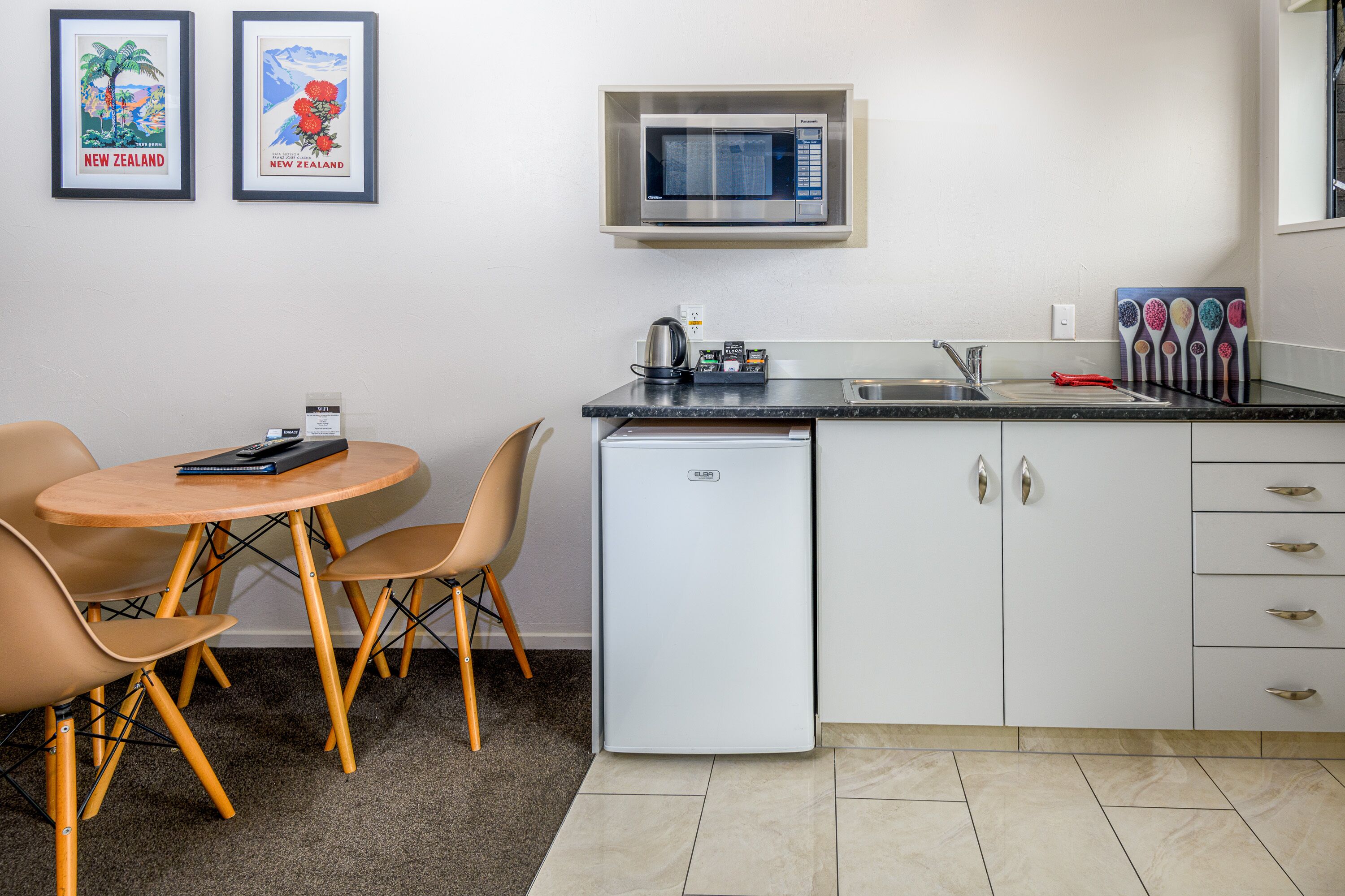 Cocina compacta con microondas, un refrigerador pequeño, un lavamanos y una zona de comedor con mesa y sillas.