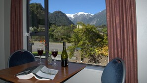 A table with a menu, two wine glasses, and a bottle of wine, set against a window with a mountain view.