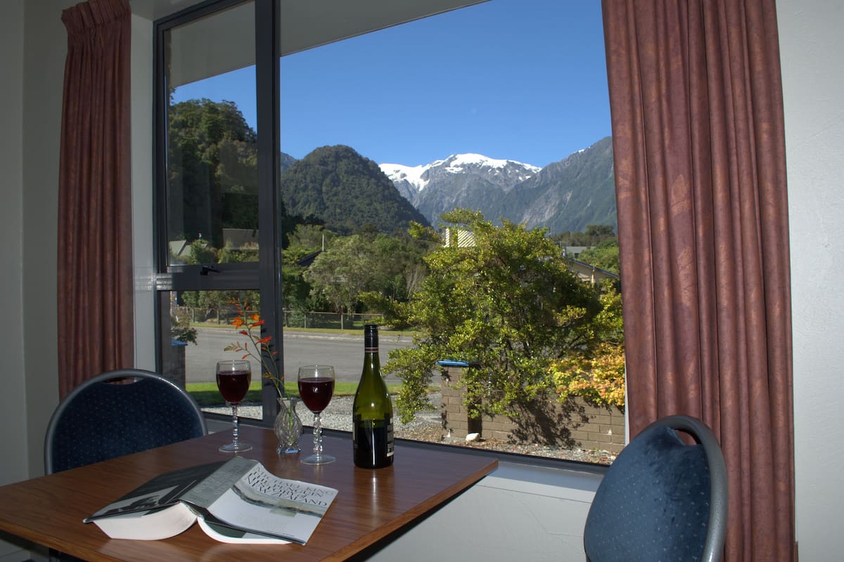 A table with a menu, two wine glasses, and a bottle of wine, set against a window with a mountain view.