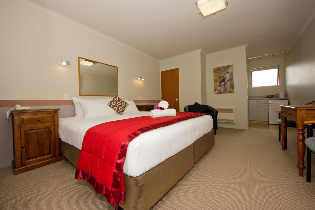 A hotel room with a large bed, a wooden nightstand, a desk, and a mirror.