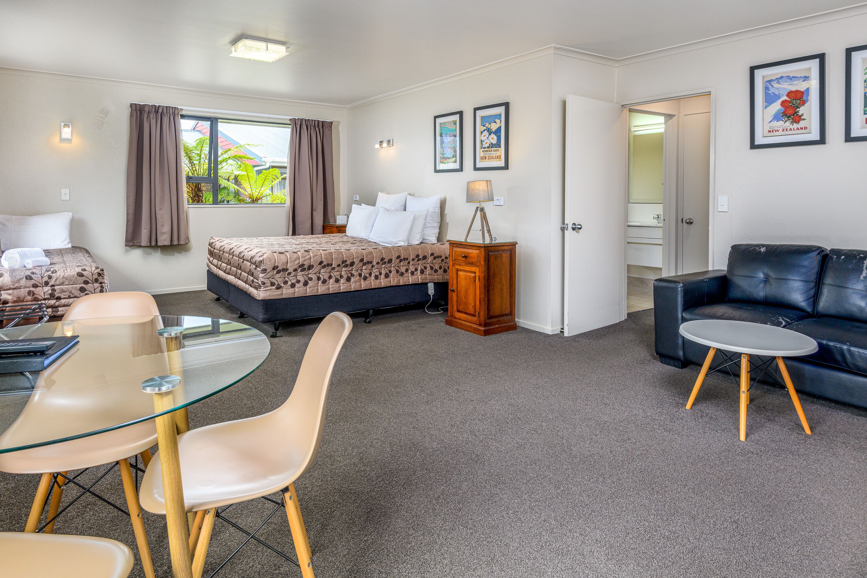 Una habitación de hotel moderna con una cama, una mesa de comedor de vidrio, un sofá y una mesita auxiliar.