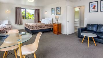 Una habitación de hotel moderna con una cama, una mesa de comedor de vidrio, un sofá y una mesita auxiliar.