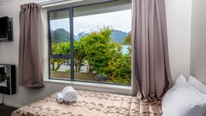A hotel room with a bed, a window with curtains, a TV, and a view of mountains and trees.