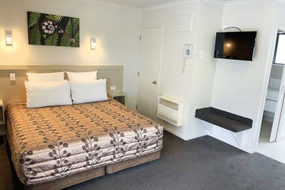 A hotel room with a bed, a mounted TV, a small shelf, and a door.