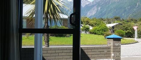 A view through a glass door of a building with a mountain backdrop, a palm tree, and a brick wall.