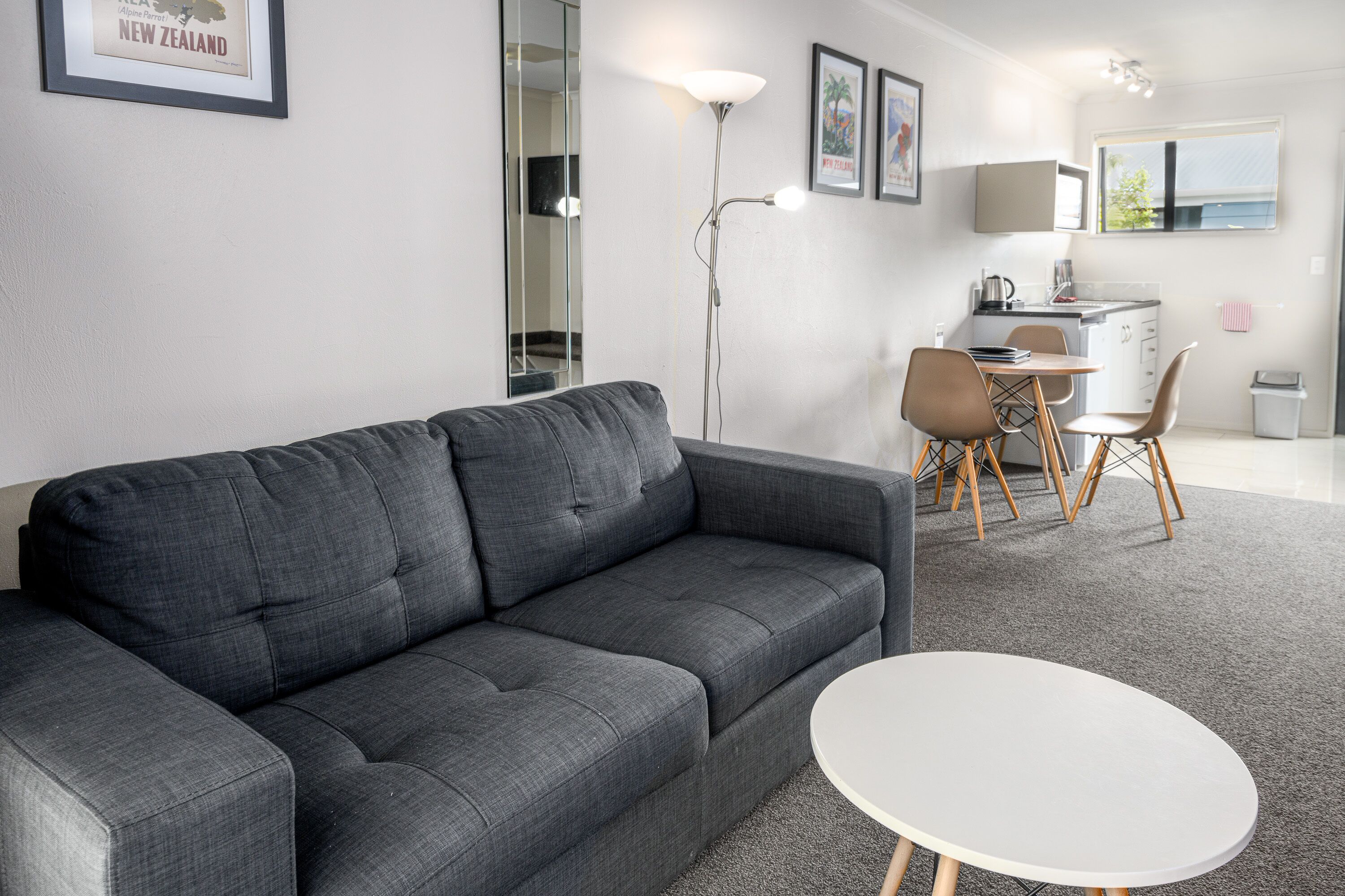 Een moderne woonkamer met een grijze bank, een witte salontafel, en een eethoek met een kleine tafel en stoelen.