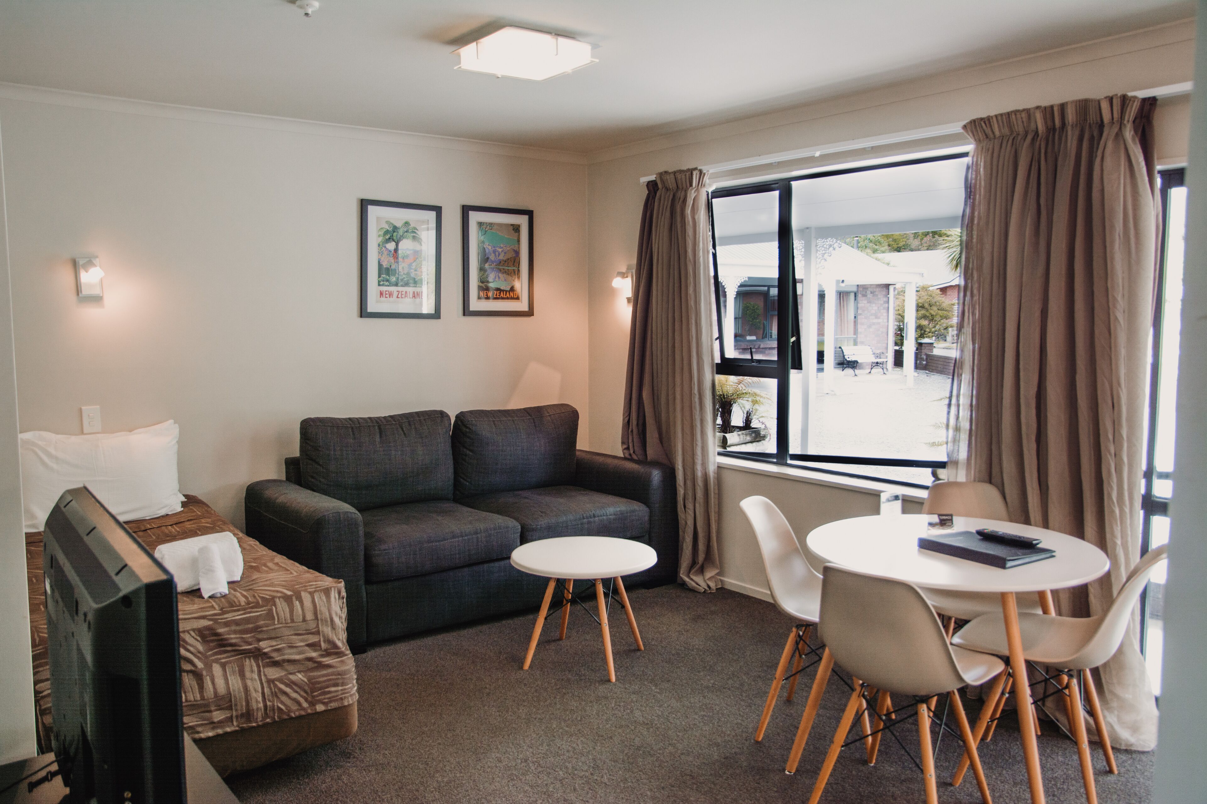 A hotel room with a sofa, a small table with chairs, a TV, and two framed pictures on the wall.