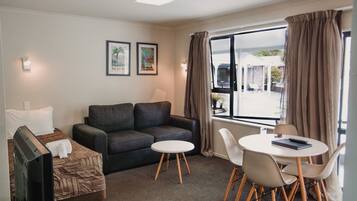 A hotel room with a sofa, a small table with chairs, a TV, and two framed pictures on the wall.
