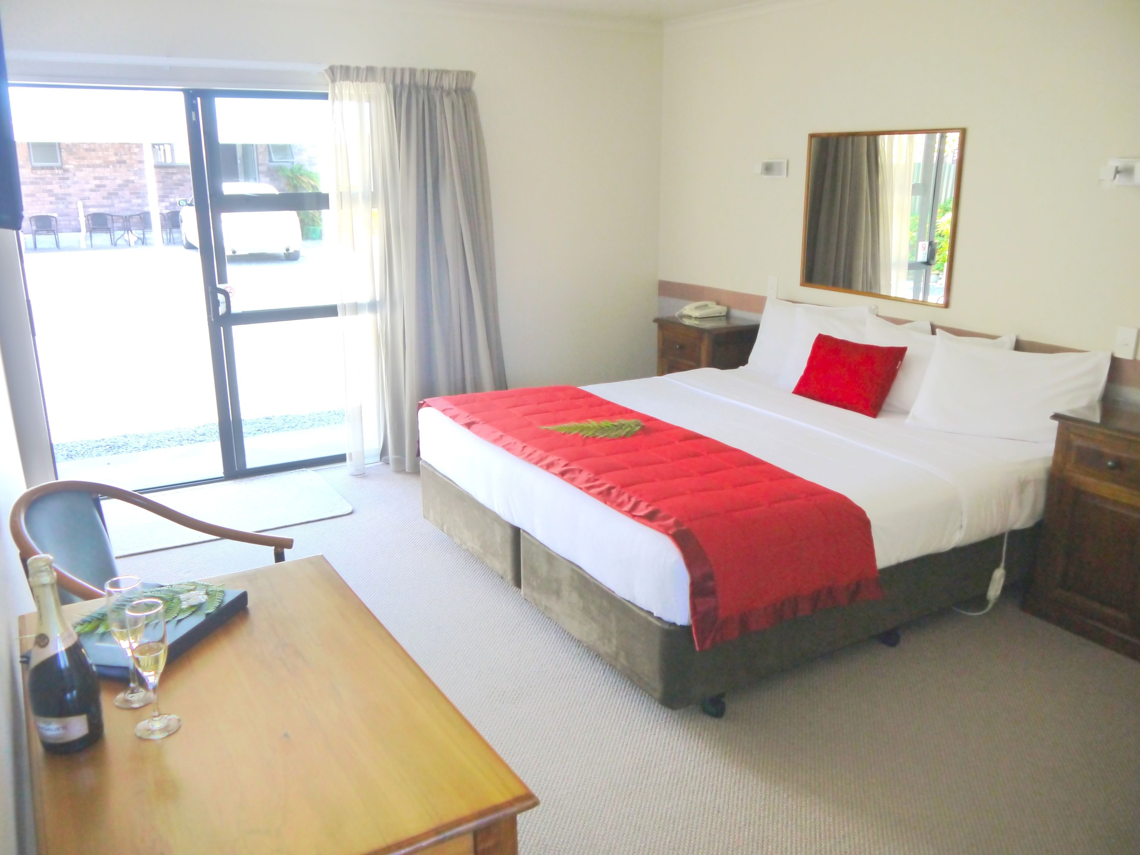 Habitación de hotel con cama, escritorio, silla, mesita de noche, espejo y ventana con cortinas.