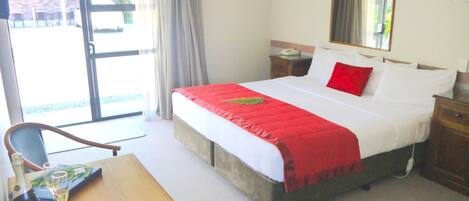 Habitación de hotel con cama, escritorio, silla, mesita de noche, espejo y ventana con cortinas.