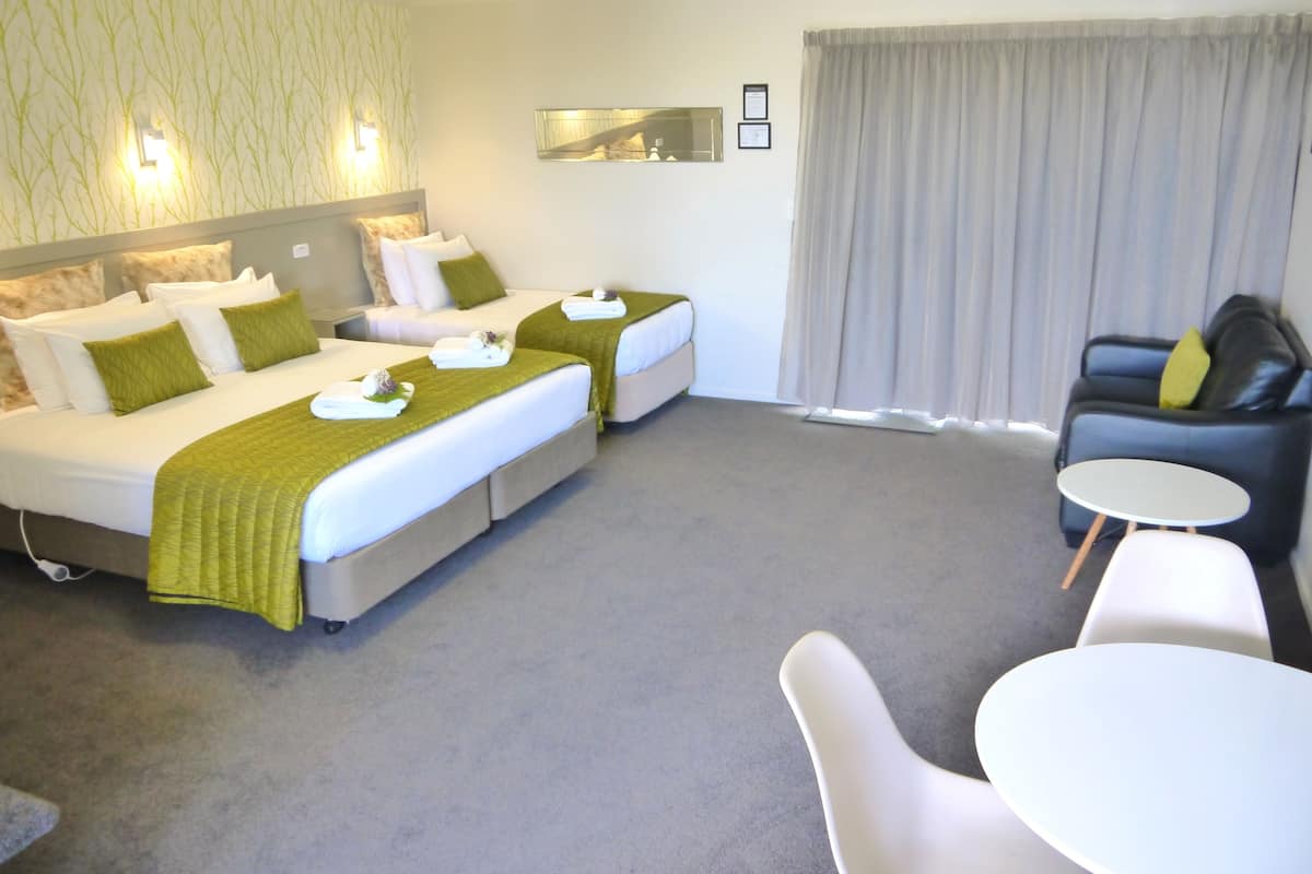 A hotel room with two beds, a sofa, a small table, and a large window with curtains.