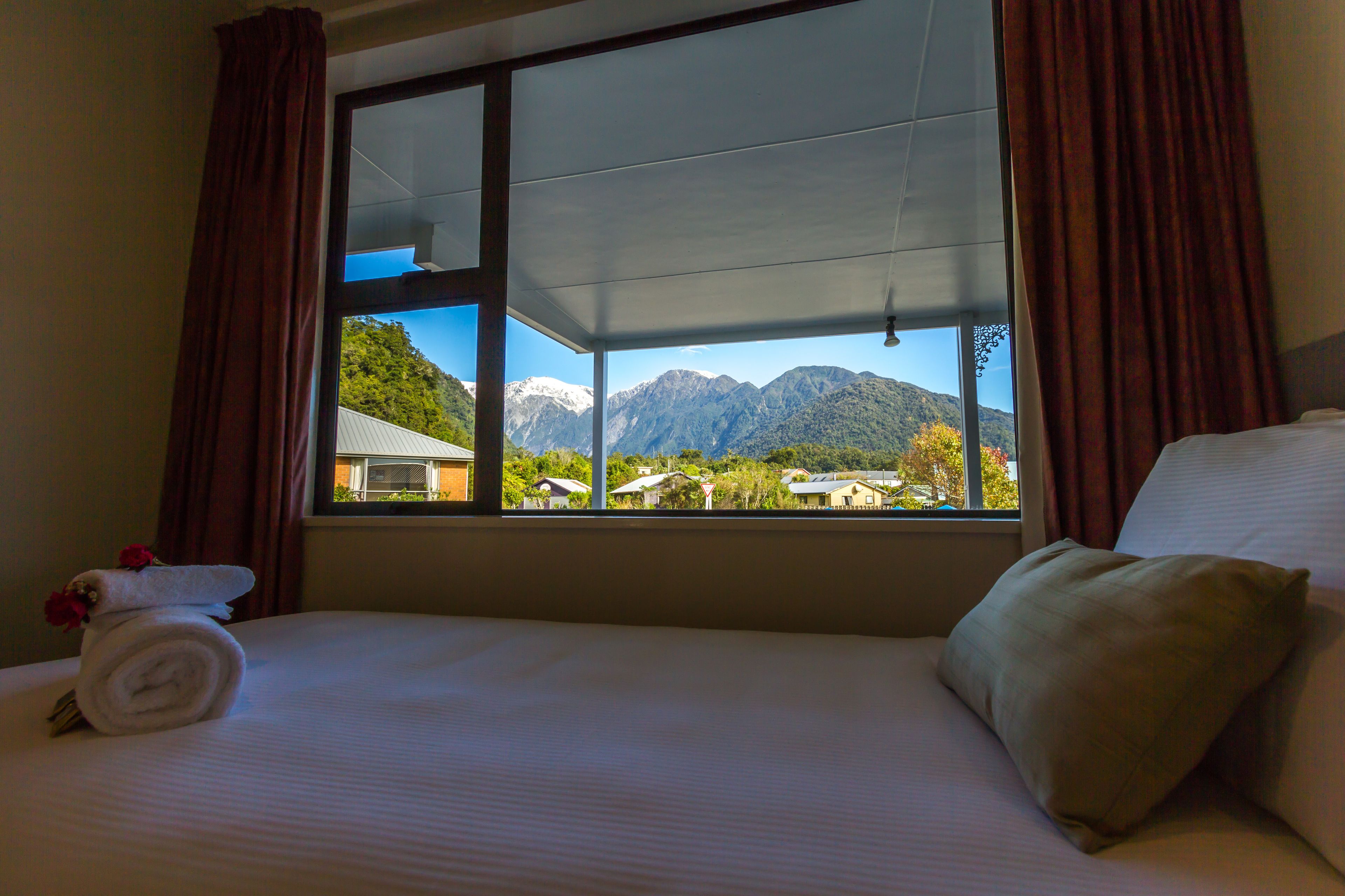 A hotel room with a bed, a window with a mountain view, and a towel with a flower.