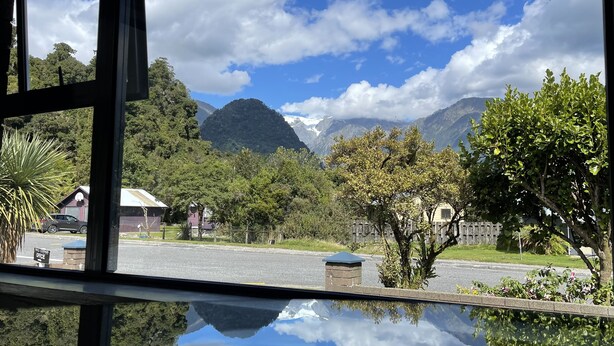 A view from inside a building, looking out to a street with houses, trees, and mountains in the background.