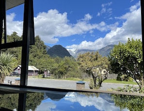 A view from inside a building, looking out to a street with houses, trees, and mountains in the background. - The Terrace (Franz Josef Glacier)