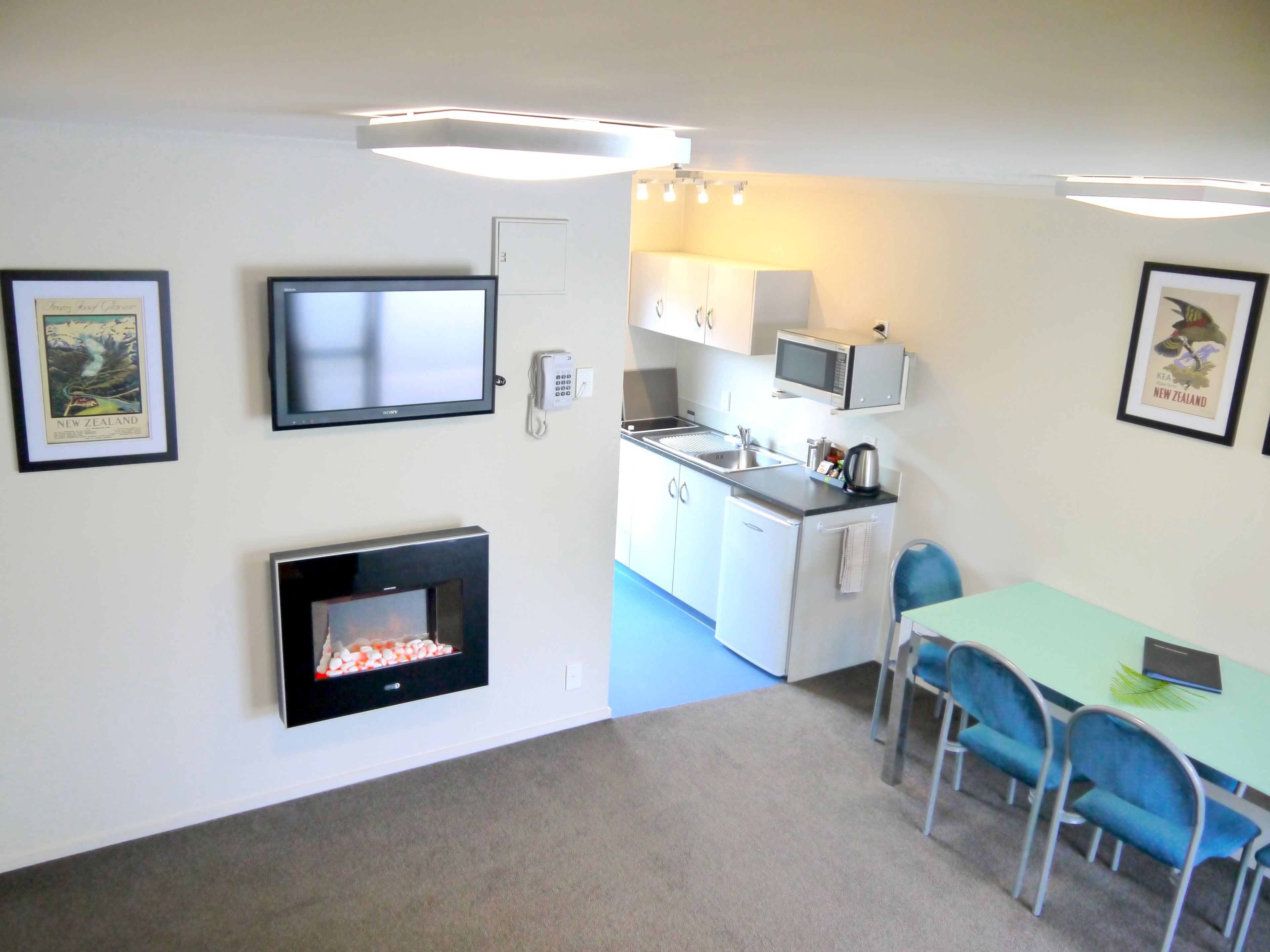 A compact living space with a kitchenette, a dining area with blue chairs, a flat-screen TV, and a fireplace.