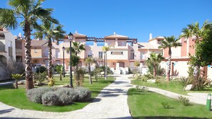 Un patio con un sendero, palmeras y un edificio con balcones.