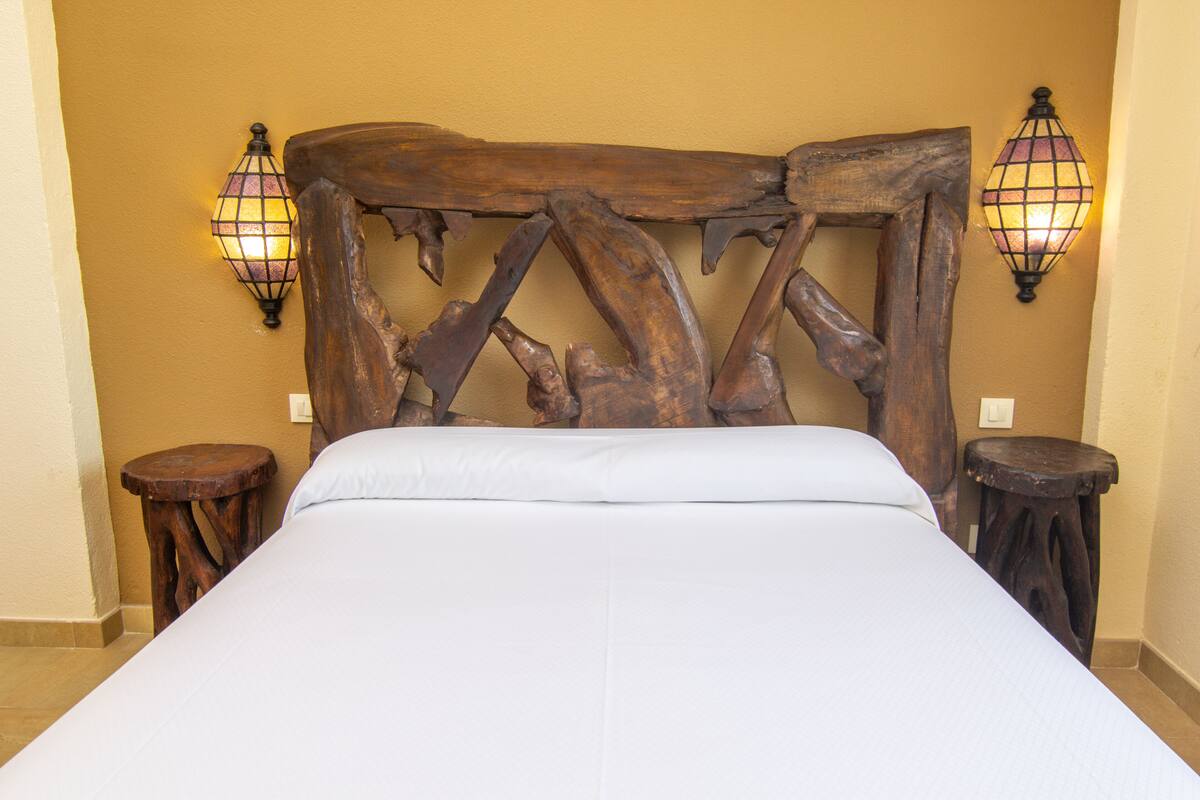 A bed with a wooden headboard, two wooden nightstands, and wall-mounted lamps.