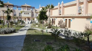 Un barrio residencial con un camino pavimentado, palmeras y un edificio con techo de tejas.