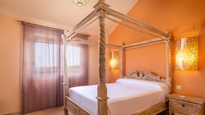 Una cama con dosel de madera y ropa de cama blanca, una mesita de noche con un jarrón, y una lámpara de pared.