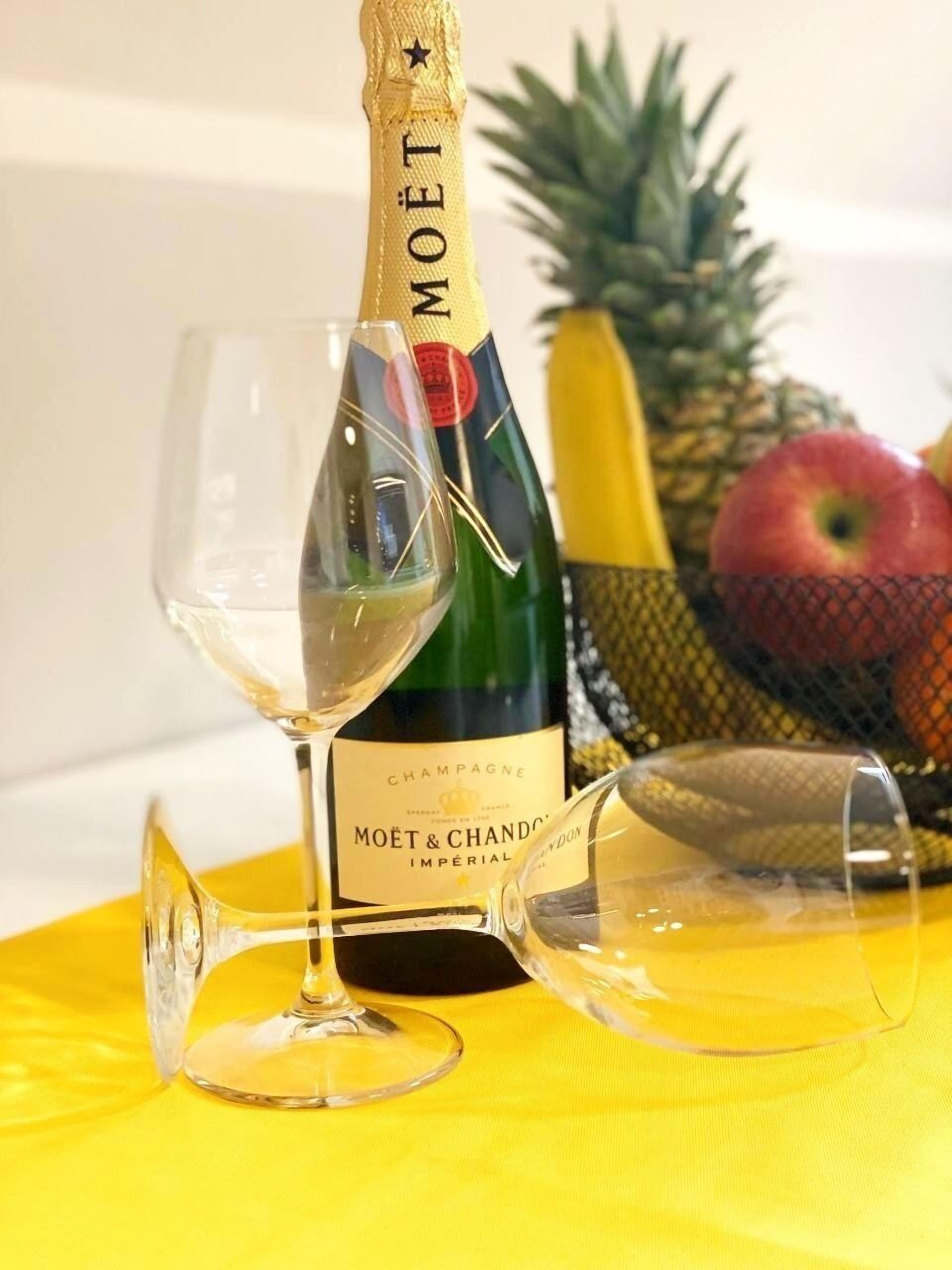 Una botella de champán Moët & Chandon con una copa y una piña sobre una mesa amarilla.