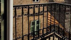 A stone building with a tiled roof, a metal balcony railing, and a clear sky with sunlight. - D & Sons Apartments (Kotor)