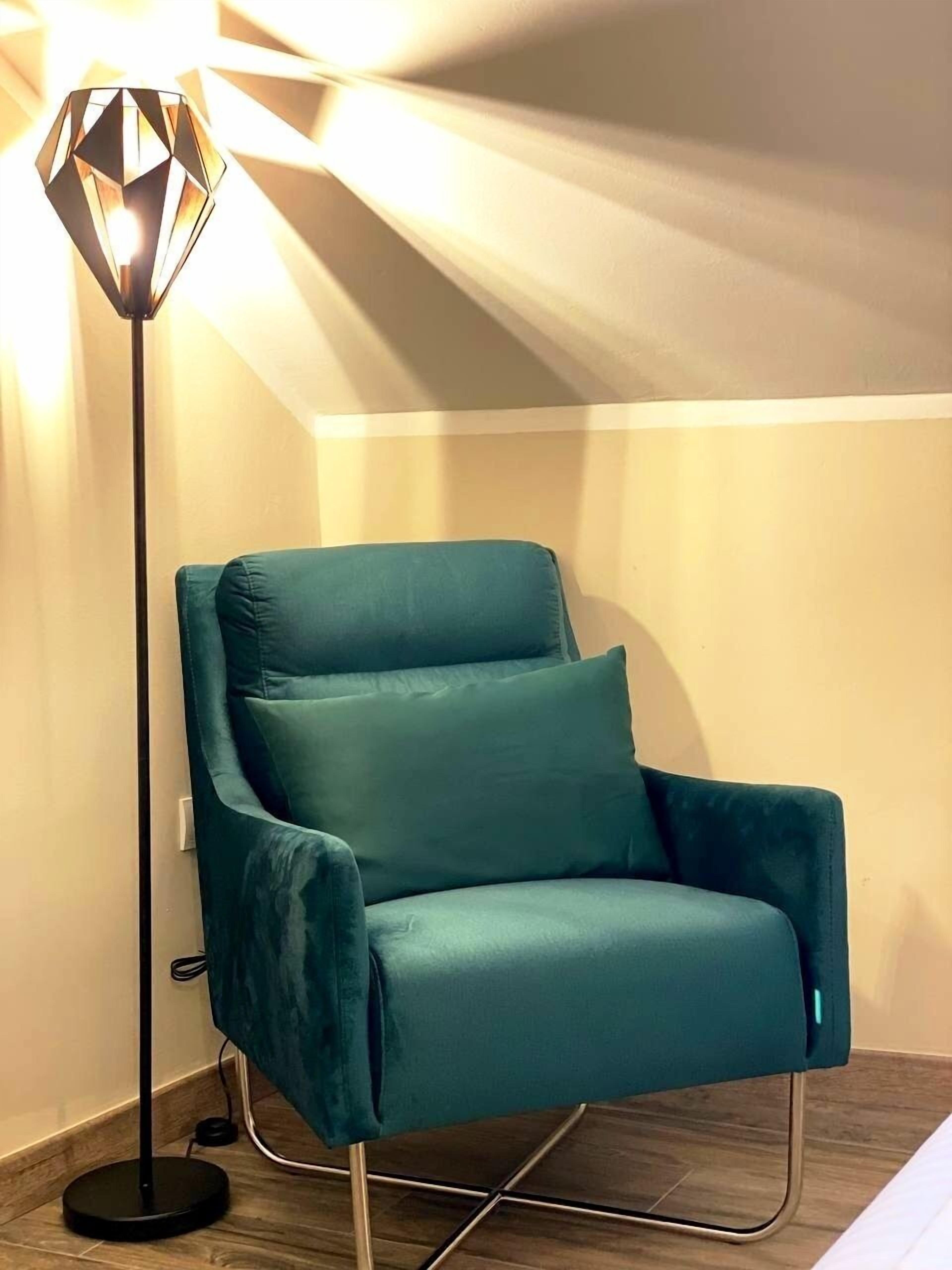 Ein türkisfarbener Sessel mit Metallgestell, neben einer Stehlampe mit geometrischem Design.