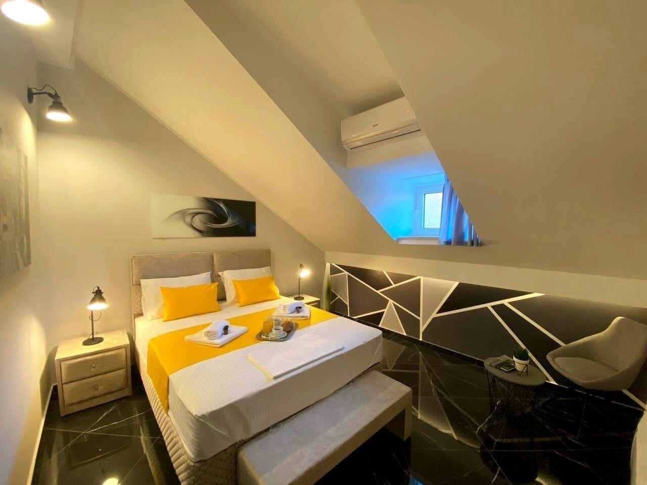 A modern bedroom with a bed, bedside tables, a bench, a chair, and a geometric wall design.