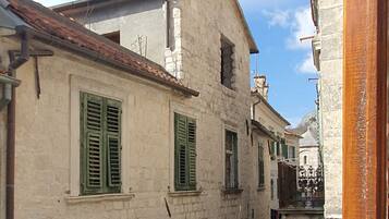 A narrow street with buildings featuring arched doorways and green shutters.