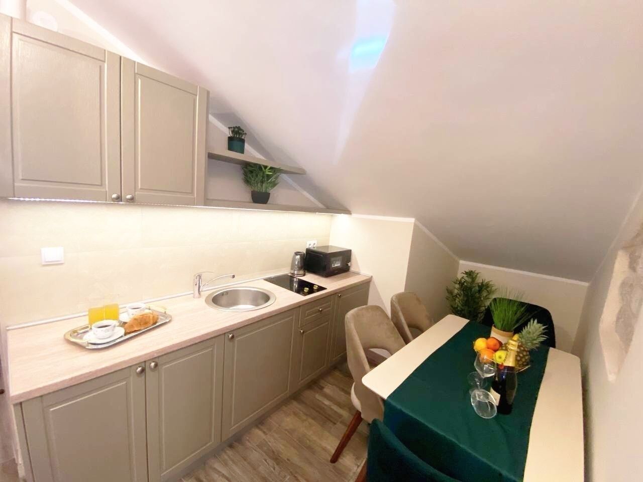 A compact kitchen with a sink, a microwave, and a tray with food. There is a dining table with chairs and a green tablecloth.