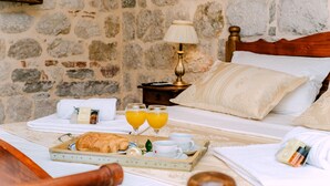 A neatly made bed with a wooden headboard, a tray with croissants and juice glasses, and a nightstand with a lamp and a small box. - D & Sons Apartments (Kotor)