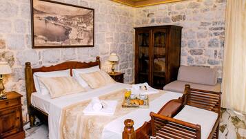 A hotel room with stone walls, a large bed with a wooden headboard, a wooden cabinet, and a framed picture on the wall.