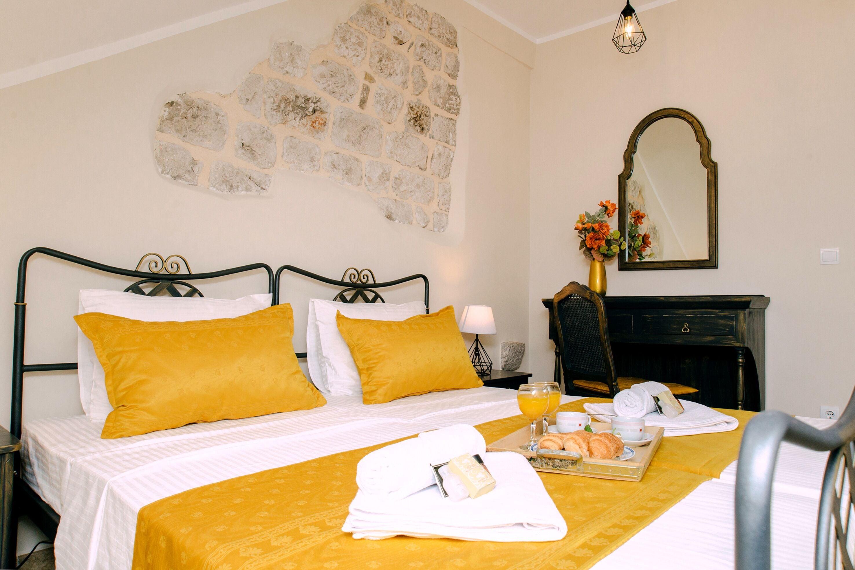 A hotel room with a bed, a breakfast tray, a mirror, and a stone wall.