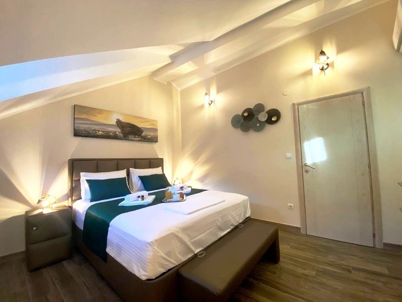 A modern hotel room with a bed, bedside tables, a bench, a wall-mounted artwork, and a door.