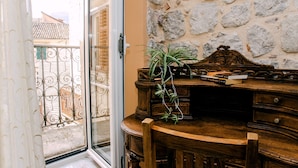 A room with a wooden desk, a potted plant, and a stone wall. - D & Sons Apartments (Kotor)